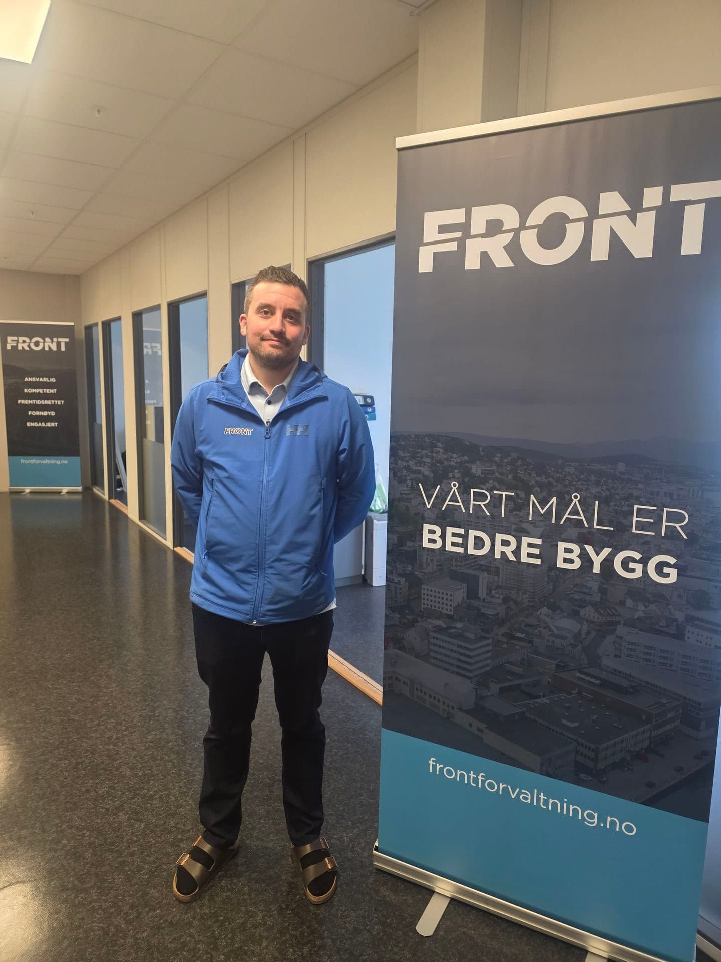 Ansatt i Front Forvaltning i Helly Hansen-jakke med Front-logo på brystet, foran bedriftens roll-up