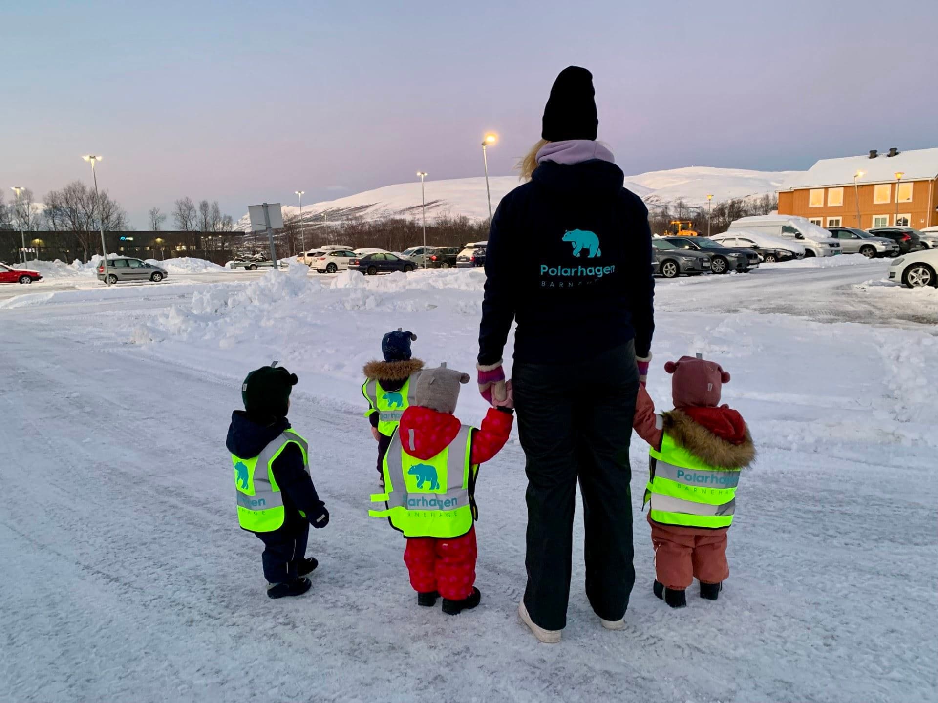 Ansatt i Polarhagen Barnehage på tur med fire barn i refleksvester med barnehagens logo